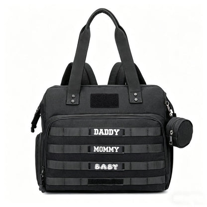 black tactical diaper bag tote showing front zipper compartment horizontal webbing patch panels and side accessory pouch