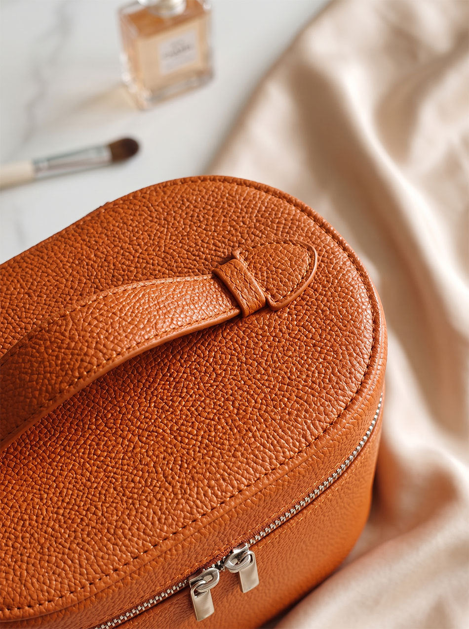 brown structured makeup organizer case close-up showing stitched top carrying handle and textured surface